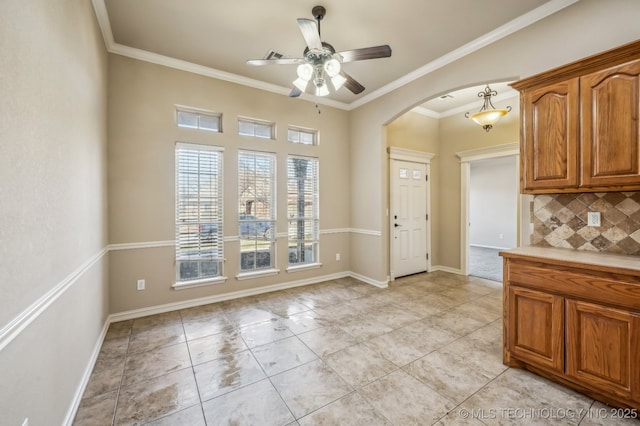 unfurnished dining area featuring baseboards, arched walkways, ceiling fan, ornamental molding, and light tile patterned flooring