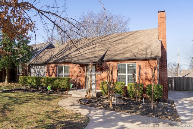 view of front facade featuring brick siding, fence, roof with shingles, a front yard, and a chimney