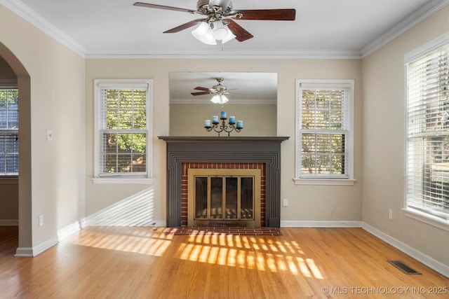 unfurnished living room featuring visible vents, a brick fireplace, ornamental molding, wood finished floors, and arched walkways