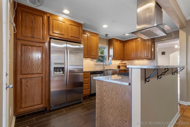 kitchen featuring decorative backsplash, island range hood, brown cabinets, and stainless steel appliances