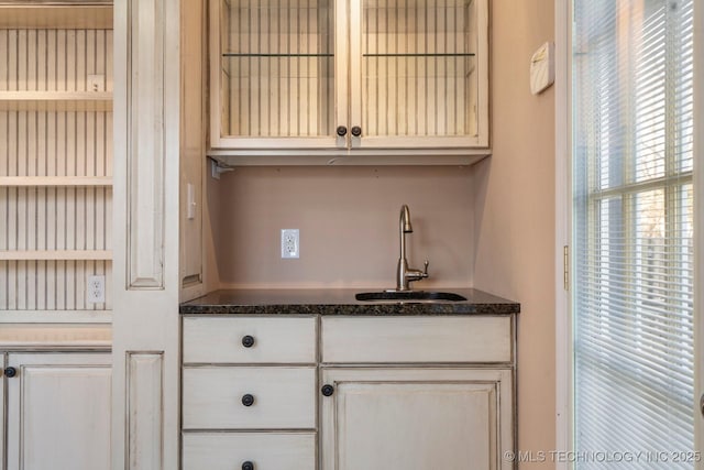 kitchen featuring a sink, open shelves, dark stone countertops, white cabinets, and glass insert cabinets