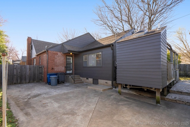 rear view of property with a shingled roof, a patio, and fence