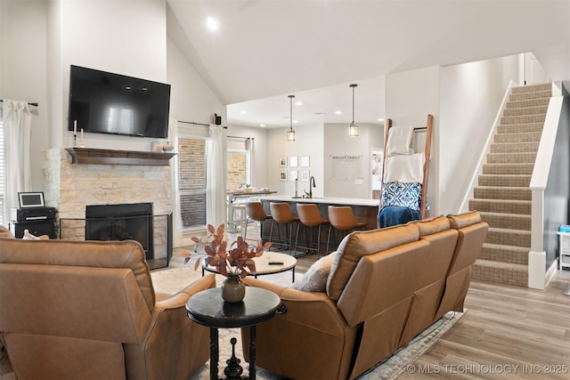 living area with light wood-style flooring, stairs, a fireplace, high vaulted ceiling, and recessed lighting