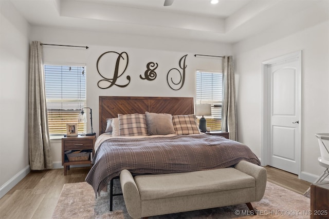 bedroom featuring light wood-style floors, baseboards, multiple windows, and a tray ceiling