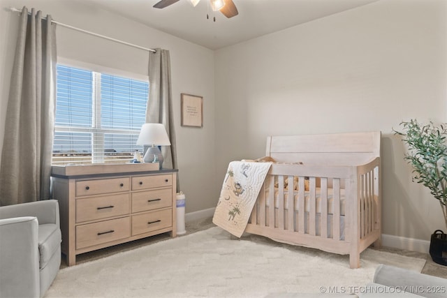 bedroom with light carpet, a crib, a ceiling fan, and baseboards