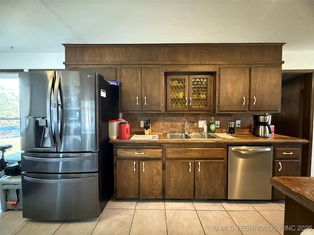 kitchen featuring light tile patterned floors, dark brown cabinetry, stainless steel appliances, a sink, and backsplash