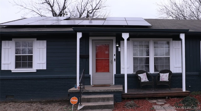 view of exterior entry with a porch, crawl space, a shingled roof, and solar panels