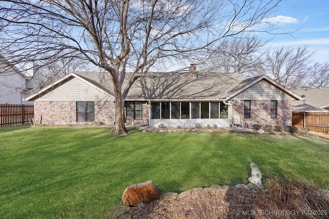 back of house with brick siding, a yard, a chimney, a sunroom, and fence