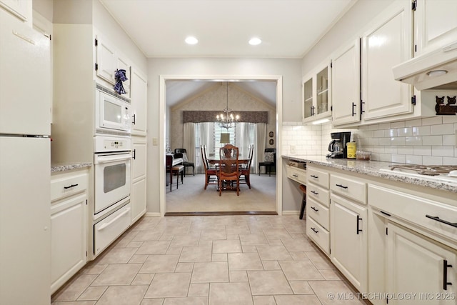 kitchen featuring white appliances, lofted ceiling, under cabinet range hood, backsplash, and a warming drawer