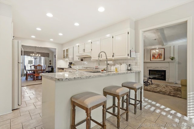 kitchen featuring decorative backsplash, a premium fireplace, freestanding refrigerator, white cabinetry, and a peninsula