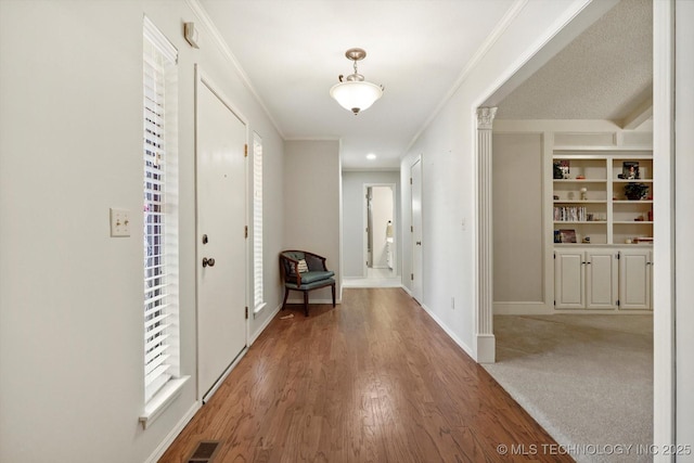 hall with light wood finished floors, visible vents, ornamental molding, plenty of natural light, and baseboards