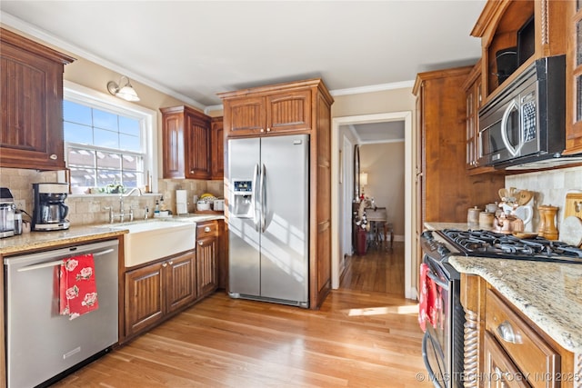 kitchen featuring crown molding, decorative backsplash, light wood-style floors, stainless steel appliances, and a sink