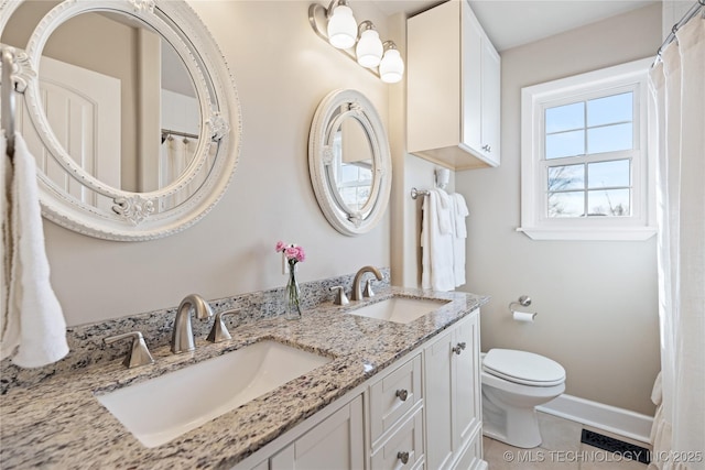 bathroom featuring double vanity, toilet, baseboards, and a sink