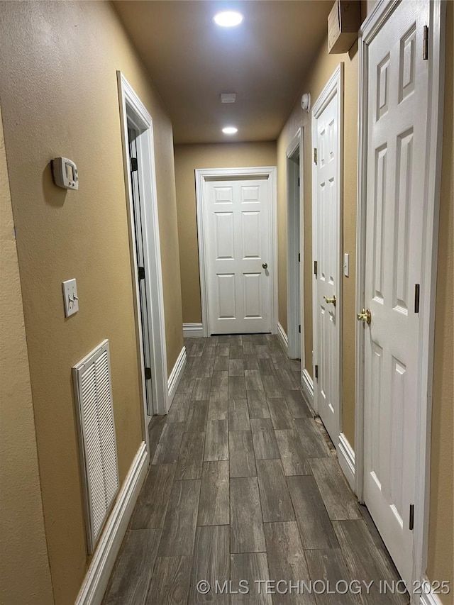 hall featuring visible vents, baseboards, and dark wood-style flooring