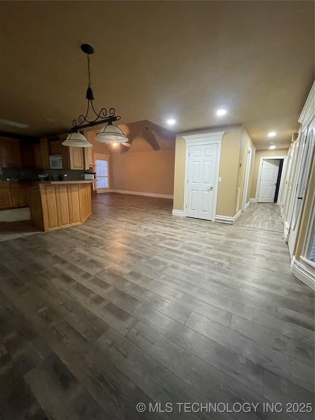 kitchen with white microwave, baseboards, decorative light fixtures, open floor plan, and wood finished floors