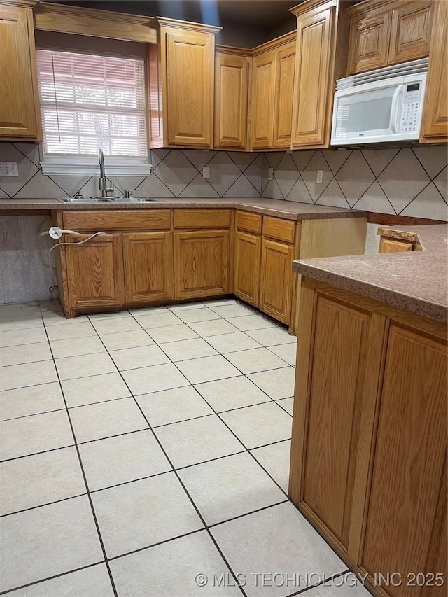 kitchen with white microwave, light tile patterned floors, decorative backsplash, and a sink