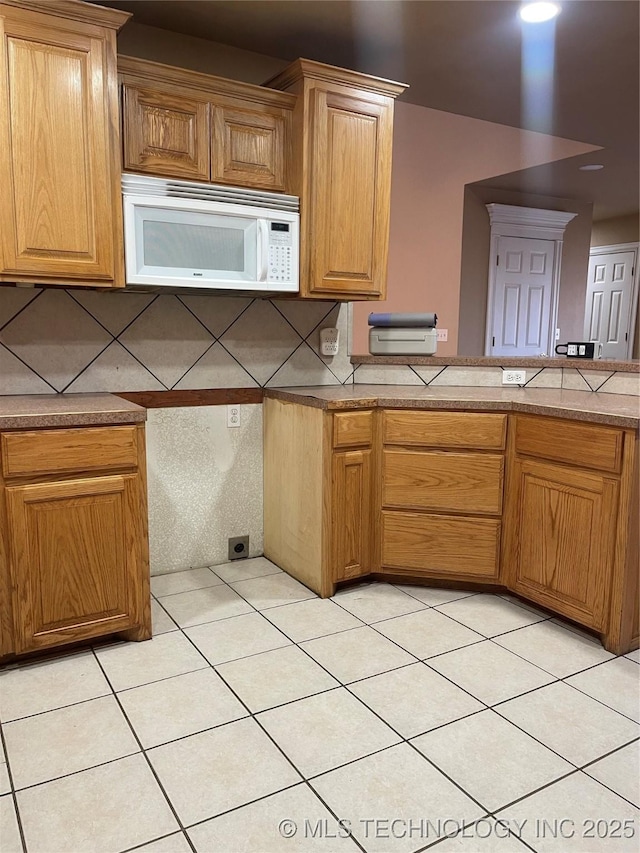 kitchen with backsplash, white microwave, and light tile patterned flooring