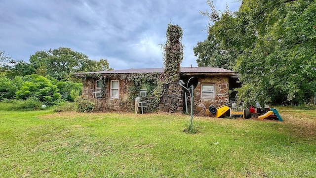 back of house featuring stone siding, a yard, and metal roof