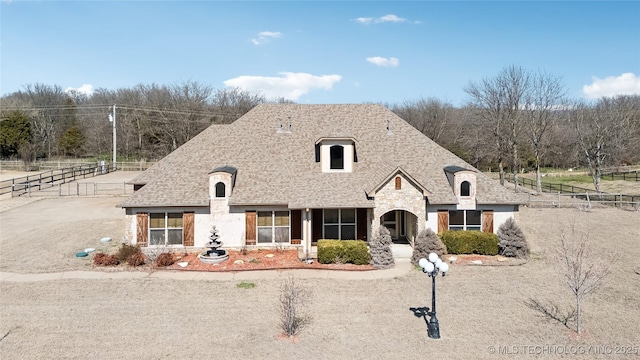 french provincial home featuring fence, stone siding, and a shingled roof