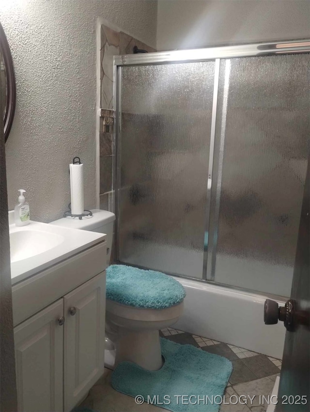 full bathroom with enclosed tub / shower combo, toilet, vanity, and a textured wall