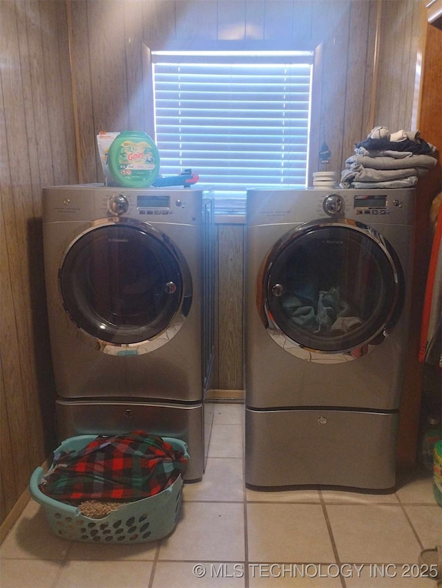 laundry area with light tile patterned floors, laundry area, washing machine and dryer, and wood walls