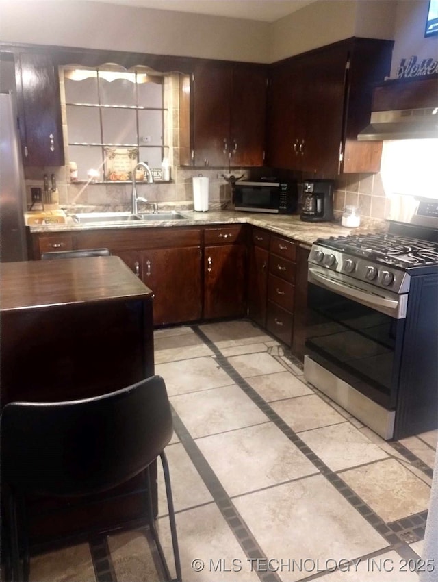 kitchen with a sink, light countertops, under cabinet range hood, appliances with stainless steel finishes, and backsplash