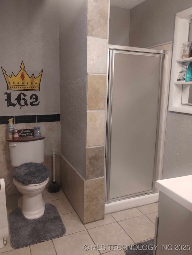 bathroom featuring tile patterned floors, toilet, tile walls, and a shower stall