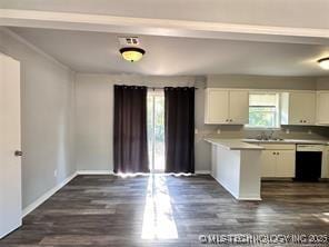 kitchen with dark wood-type flooring, baseboards, dishwasher, light countertops, and white cabinetry