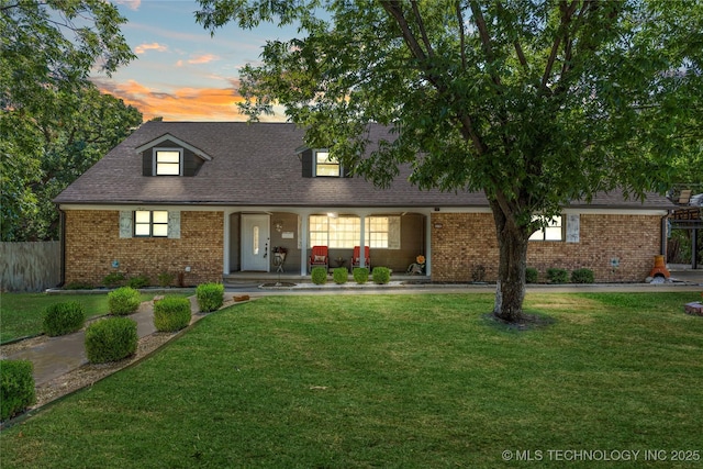 view of front of house with brick siding, a porch, a front lawn, and roof with shingles