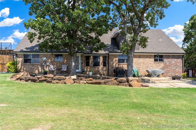 back of house featuring a lawn, fence, a shingled roof, brick siding, and a patio area