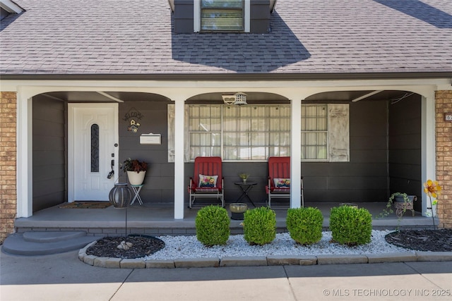 entrance to property with a porch, brick siding, and roof with shingles