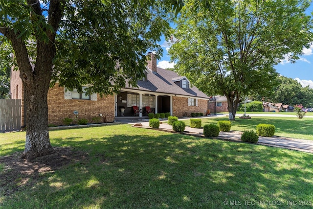 view of front of home with a front lawn, fence, covered porch, brick siding, and a chimney