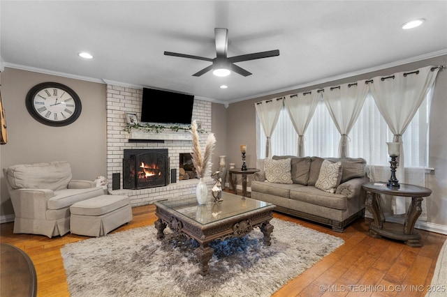 living area with a fireplace, crown molding, ceiling fan, and wood finished floors