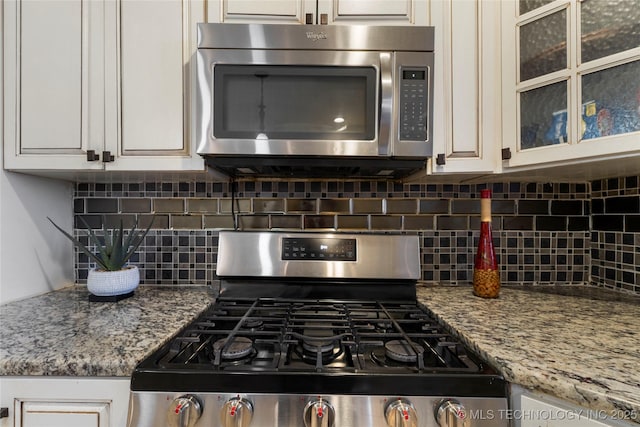 kitchen with tasteful backsplash, glass insert cabinets, light stone counters, appliances with stainless steel finishes, and white cabinetry