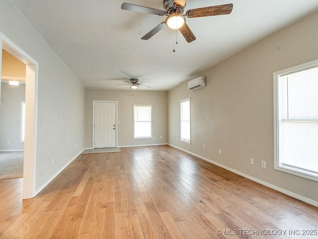 unfurnished room featuring a ceiling fan, an AC wall unit, baseboards, and light wood-type flooring