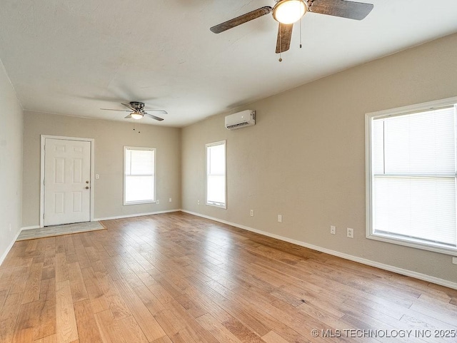 spare room with ceiling fan, baseboards, an AC wall unit, and light wood-style flooring