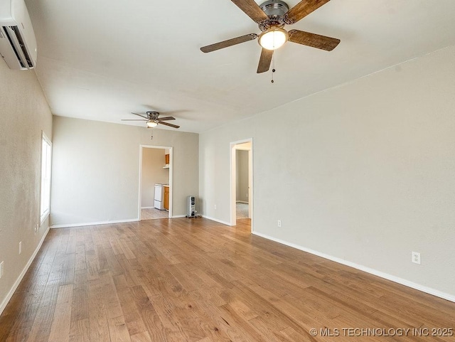 spare room featuring an AC wall unit, baseboards, and light wood finished floors