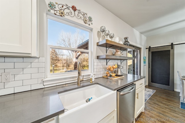 kitchen featuring tasteful backsplash, stainless steel dishwasher, dark countertops, a barn door, and white cabinets