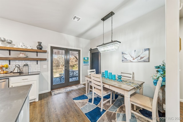 dining area featuring dark wood-style floors, visible vents, baseboards, french doors, and a barn door