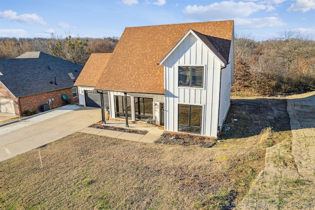 modern inspired farmhouse with driveway, cooling unit, board and batten siding, a shingled roof, and a garage