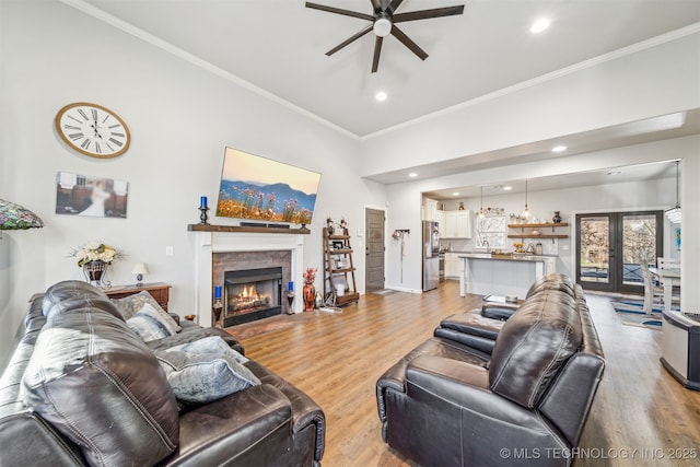 living room with a stone fireplace, crown molding, a ceiling fan, and light wood-type flooring