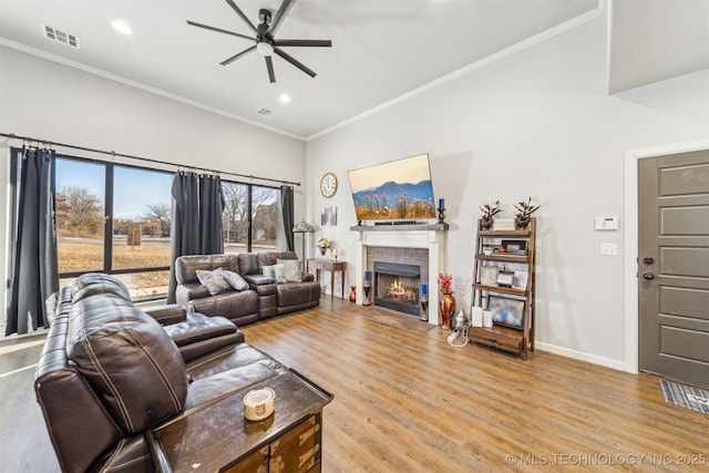 living room featuring a tiled fireplace, visible vents, crown molding, and light wood-type flooring