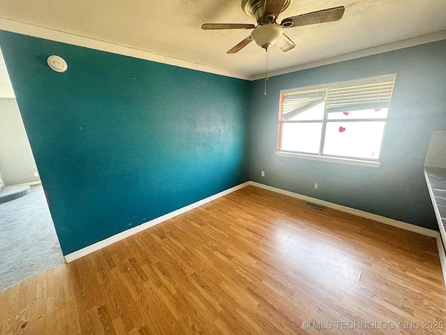 empty room with visible vents, baseboards, ornamental molding, wood finished floors, and a ceiling fan