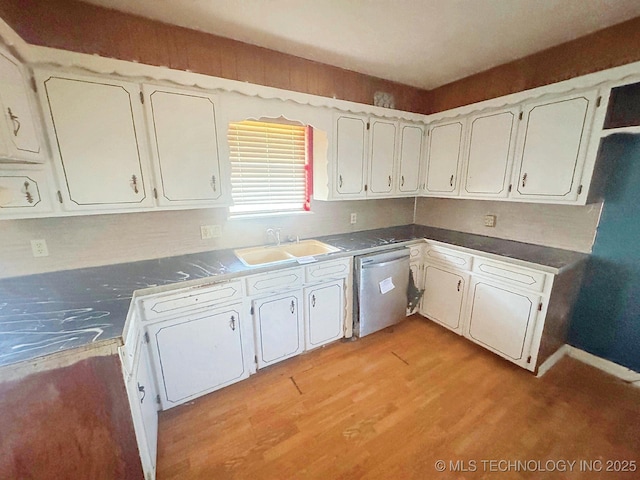 kitchen featuring a sink, white cabinets, light wood-style floors, stainless steel dishwasher, and dark countertops