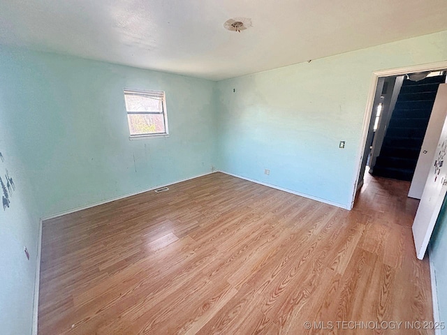 empty room with visible vents, stairs, and light wood-type flooring