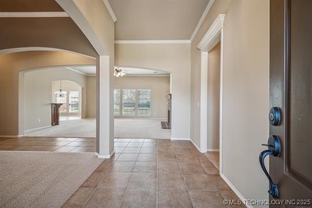 foyer featuring tile patterned floors, carpet, arched walkways, and ornamental molding