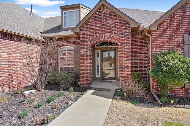 doorway to property featuring brick siding and a shingled roof