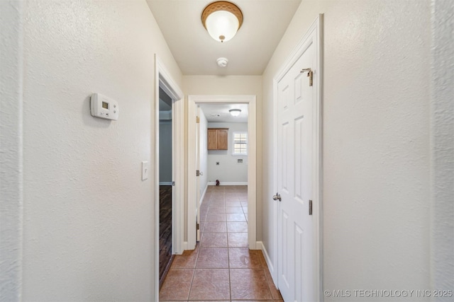 corridor with tile patterned floors, baseboards, and a textured wall