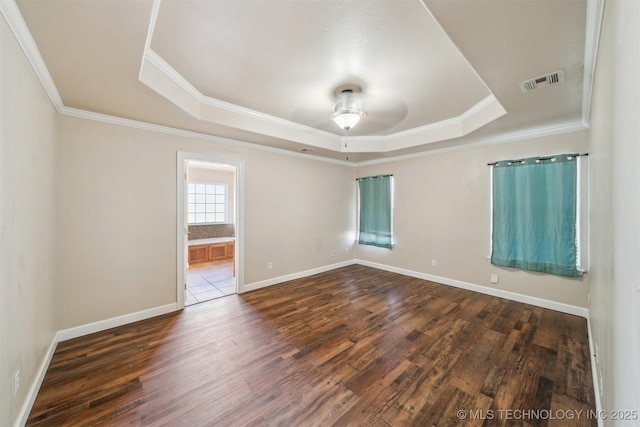 empty room with dark wood finished floors, a tray ceiling, baseboards, and visible vents