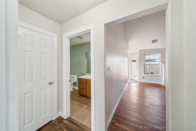 hall with visible vents, baseboards, and dark wood-style flooring